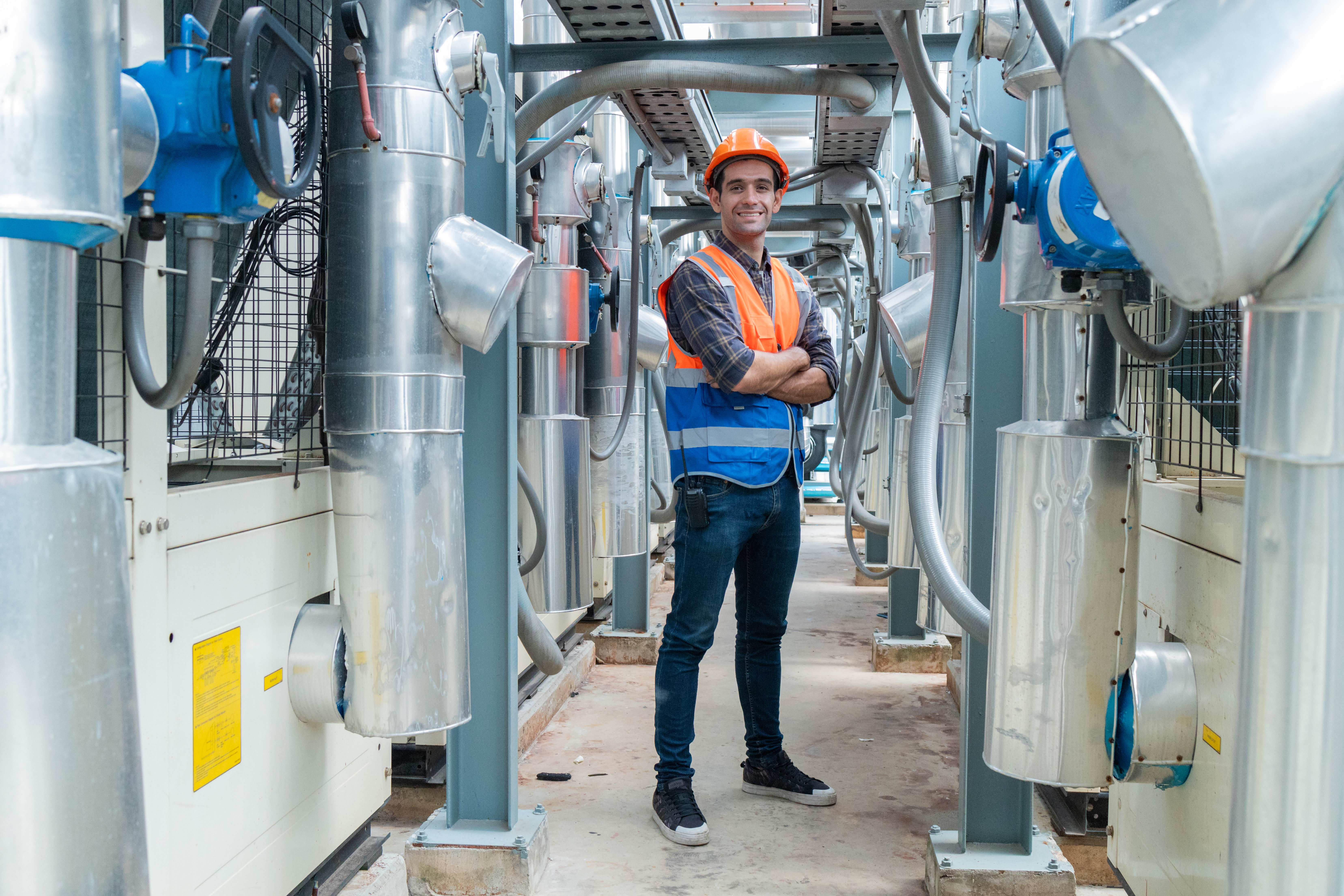 HVAC technician beside a rooftop chiller plant with insulated refrigerant piping and butterfly valves