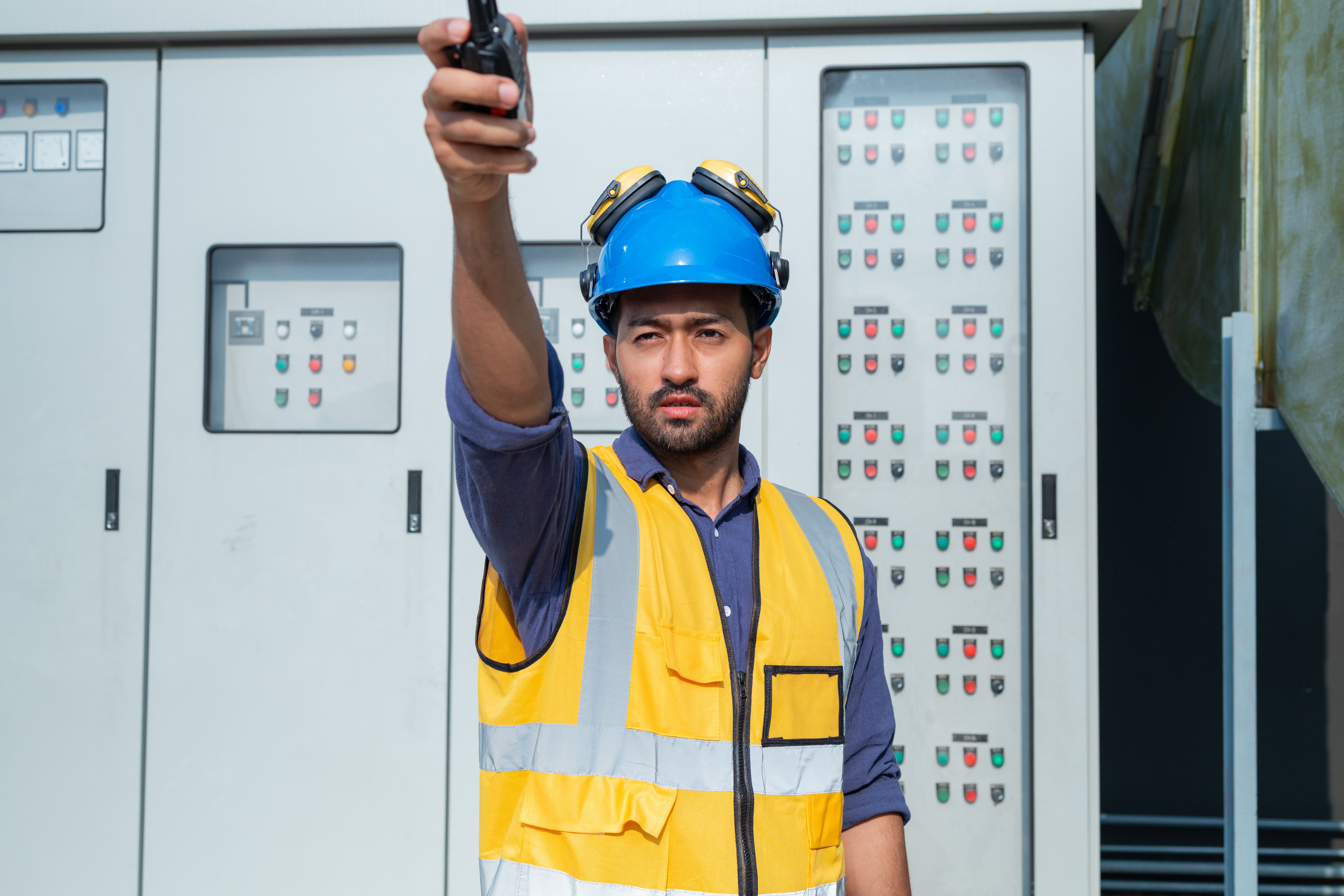 HVAC engineer with a two-way radio in front of a motor control centre panel